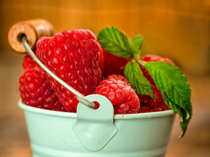 Raspberries in a small bucket with mint leaves
