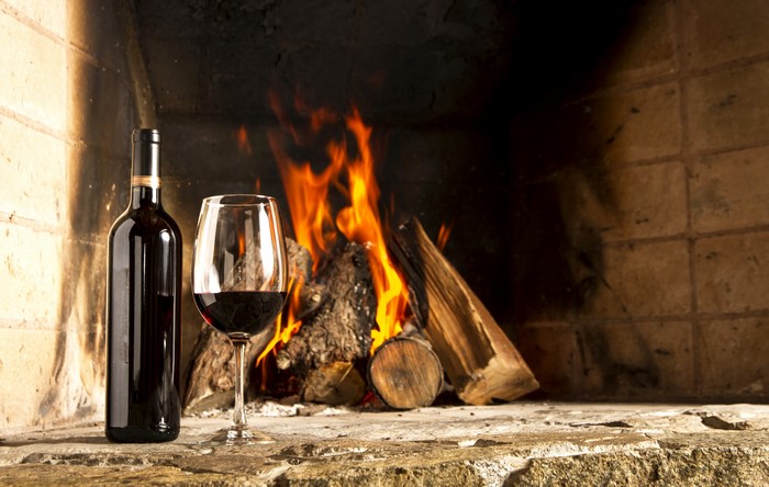 Bottle and glass of red wine by fireplace
