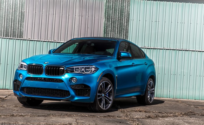 Blue BMW X6 M parked in front of a corrugated metal wall
