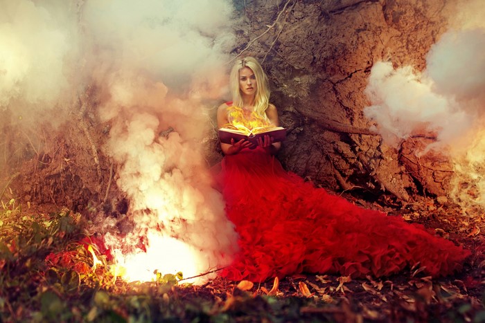 Blonde woman in red dress holding a burning book