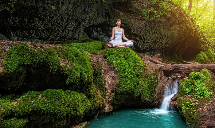 Woman meditating in lotus position by mossy waterfall