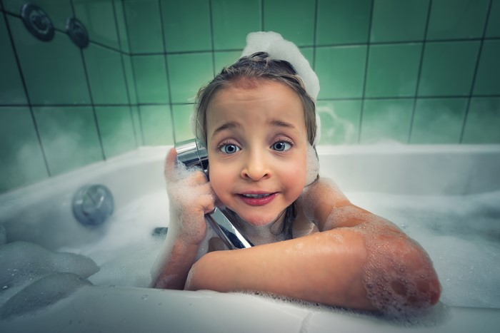 Little girl in a bubble bath holding a shower head