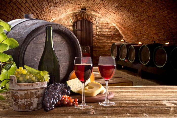 Wine cellar with barrels, grapes, cheese, and wine glasses