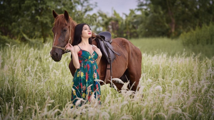 Asian woman with horse in a grassy field