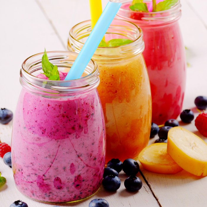 Three colorful fruit smoothies in glass jars with straws