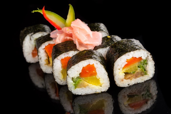 Sushi rolls with pickled ginger on black background