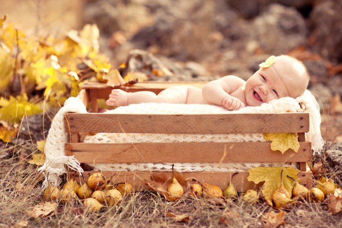Baby in a wooden crate with autumn leaves