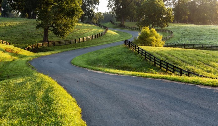 Winding Road Through Grassy Hills with Fence
