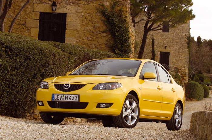 Yellow Mazda 3 Sedan parked in front of a stone building