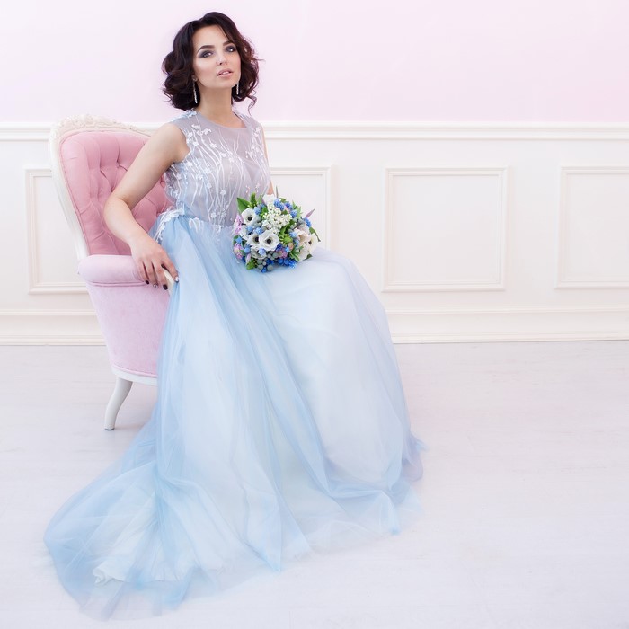 Woman in a blue dress holding a bouquet sitting in a pink armchair