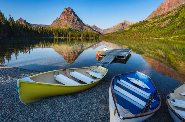 Boats on a lake with mountains reflecting in Glacier National Park, USA