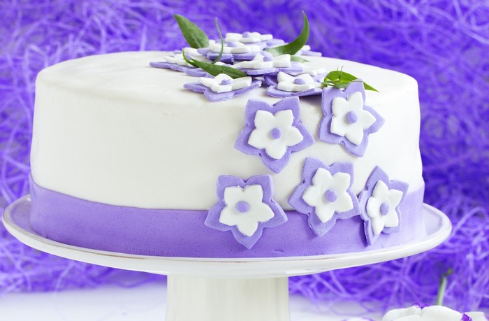 White cake with purple flowers and ribbon