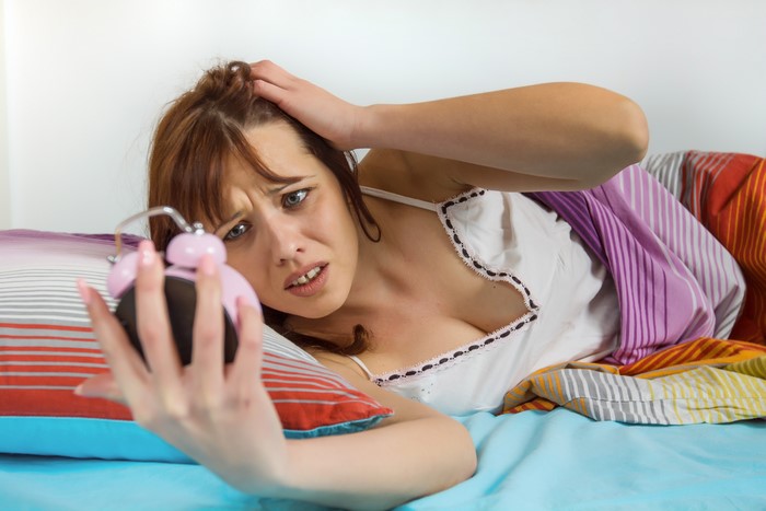 Brown-haired woman with alarm clock in bed