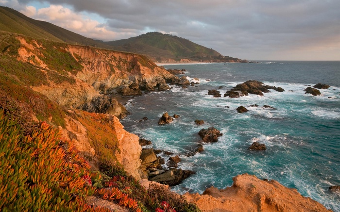 Rugged coastline with crashing waves and green hills