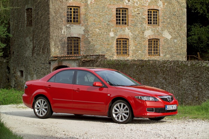 Red Mazda 6 Sedan parked near a stone building