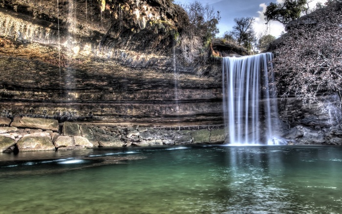Waterfall cascading into a clear pool at the base of a rocky cliff