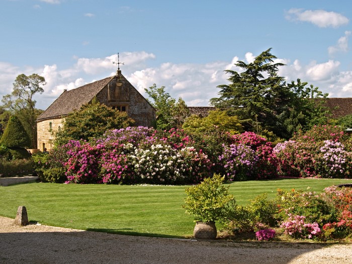 Stone building with colorful rhododendrons in a garden in England