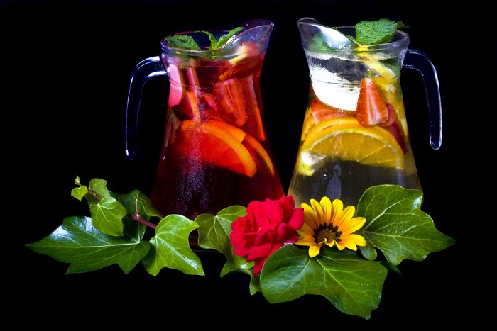 Two pitchers of fruit-infused drinks with foliage and flowers