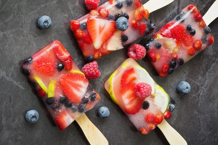 Four fruit popsicles with berries and lemon slices