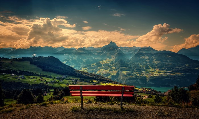 Red bench overlooking mountains and clouds