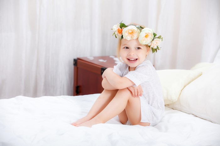 Smiling Little Girl Sitting on Bed with Flower Crown