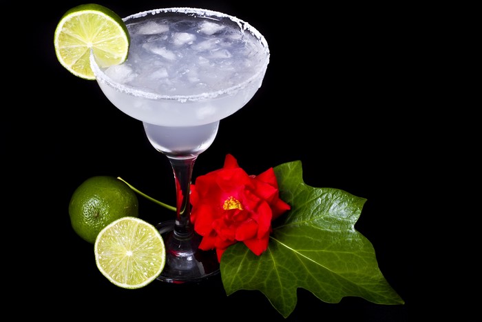 Margarita cocktail with lime and rose on black background