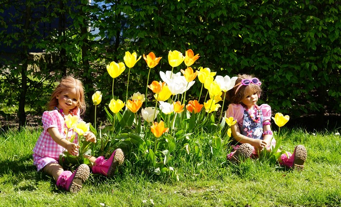 Two dolls sitting in a garden with tulips