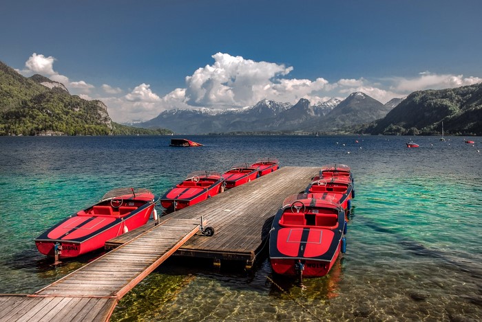 Red boats docked on a wooden pier with mountains in the background