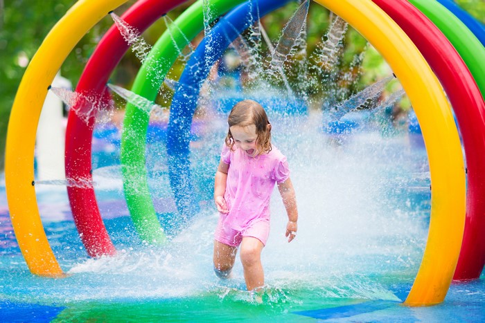Young girl playing in a water park with rainbow arches