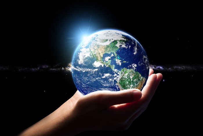 Hands holding planet Earth with sun flare and galaxy