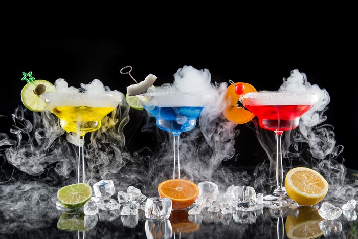 Three colorful cocktails with smoke and citrus garnishes