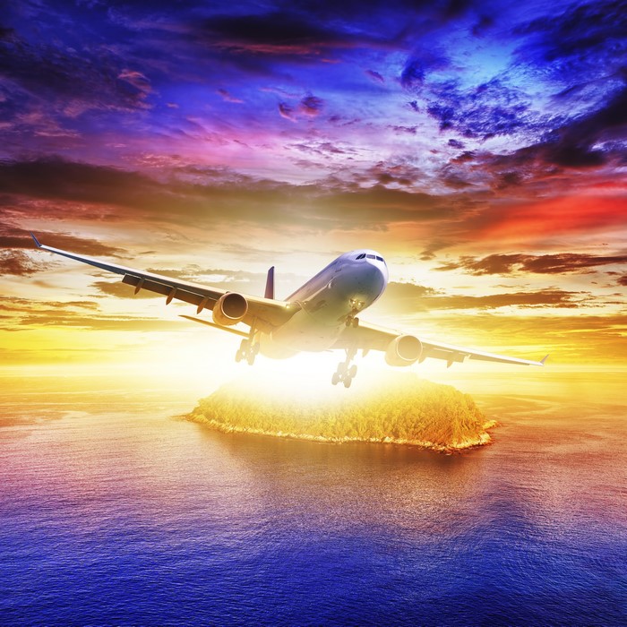 Airplane flying over island at sunset