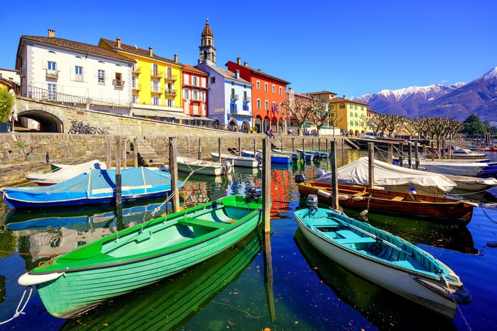 Boats docked in Ascona, Ticino, Switzerland with colorful houses and mountains
