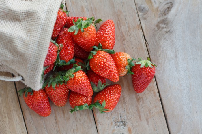 Strawberries spilling from a burlap sack onto wooden planks