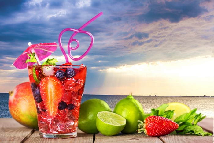 Fruit cocktail with strawberry, lime, and mango on a beach