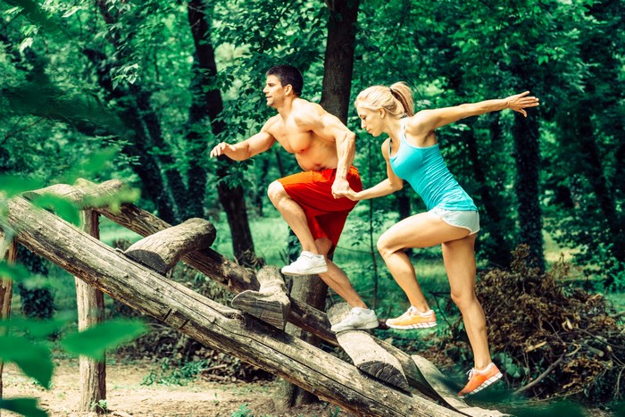 Man and woman running on wooden obstacle