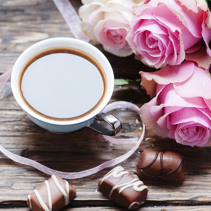 Coffee cup with roses and chocolates on wooden table