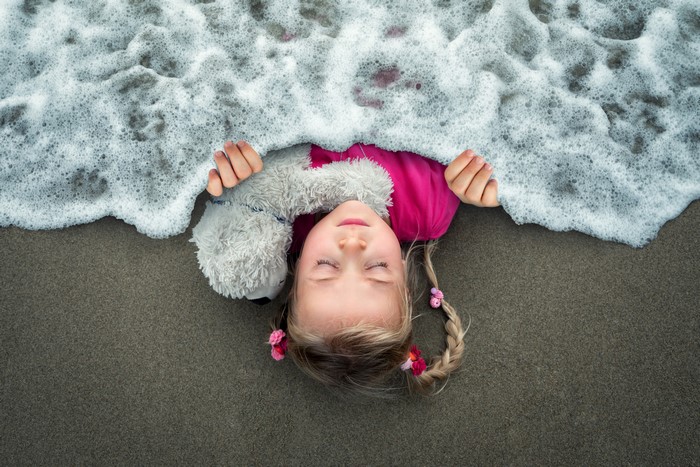 Little girl sleeping on beach with teddy bear and waves