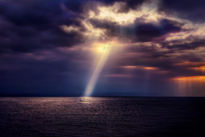 Sailboat in the sea under dramatic cloudy sky with sun rays