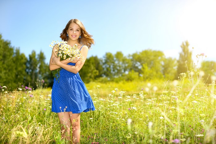 Girl in blue dress holding camomiles in a field