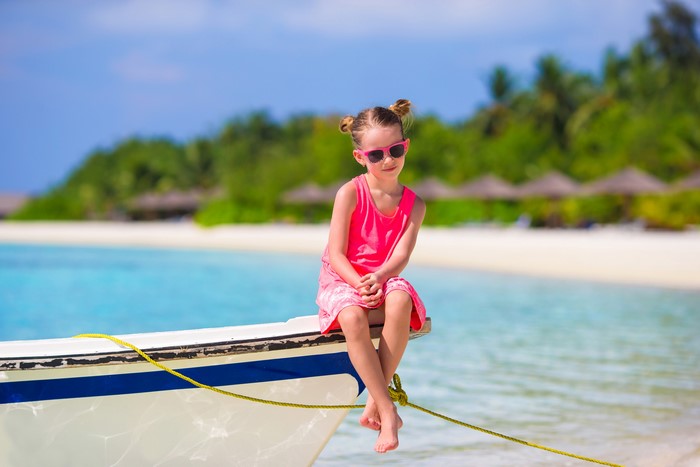 Girl in pink dress sitting on a boat at the beach