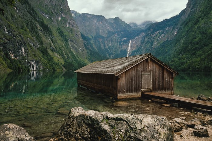 Wooden boathouse on a clear lake with mountains and waterfall