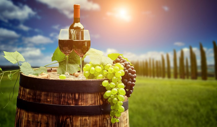 Wine bottle and glasses on barrel with grapes