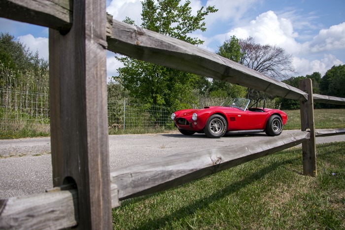 Red 1964 Cobra 289 Cabriolet by a wooden fence