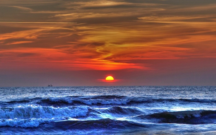 Sunset over the ocean with waves and a distant boat