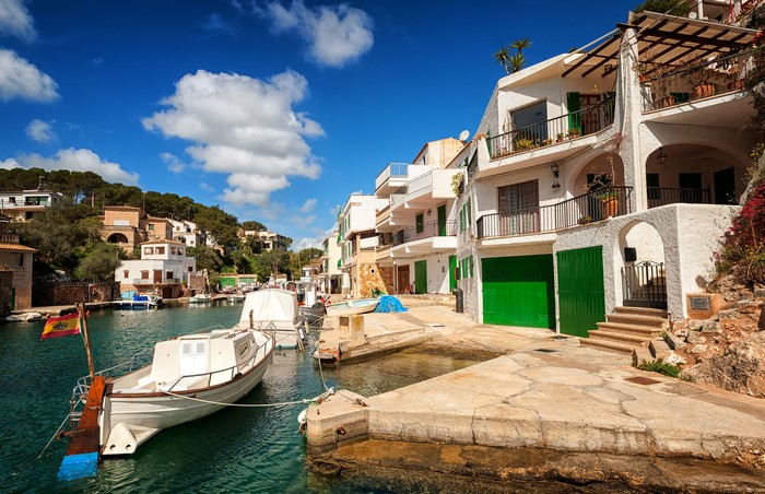 Boats docked in a harbor with white houses in Cala Figuera, Spain