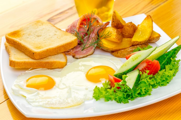 Fried eggs with toast, bacon, potatoes, and salad