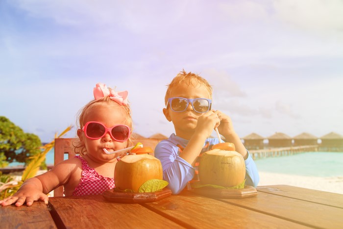 Two children drinking coconut water on a tropical beach