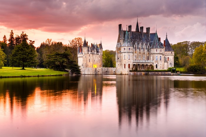 Chateau de la Bretesche castle reflected in a pond at sunset