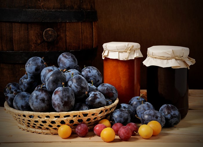 Plums and jam jars next to a wooden barrel